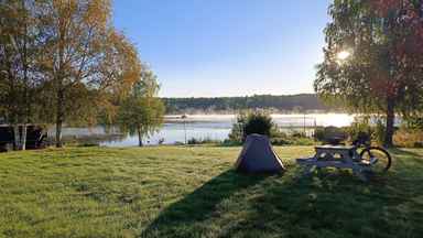 Bikepacking Schweden Zelt, Fahrrad und Picknicktisch auf einer Wiese am Seeufer bei Sonnenaufgang – Bikepacking Schweden am frühen Morgen.